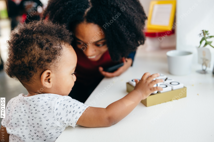 Mother works on laptop as her child sits beside