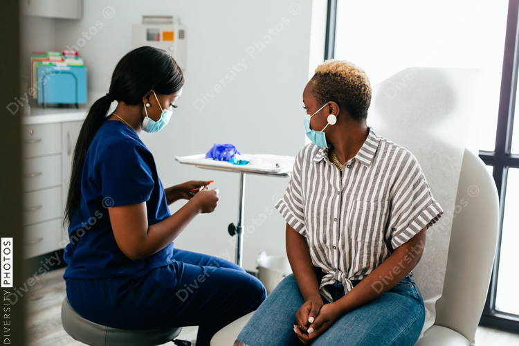 Black nurse collects blood sample from black female patient in exam room at medical facility