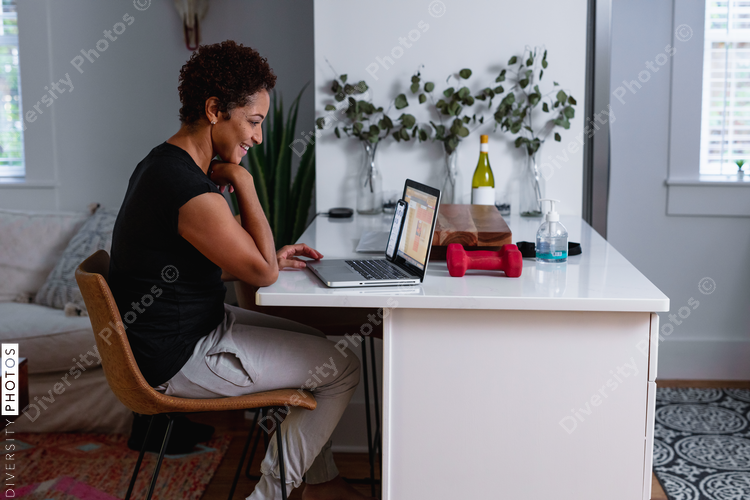 African-American woman works on laptop in home kitchen