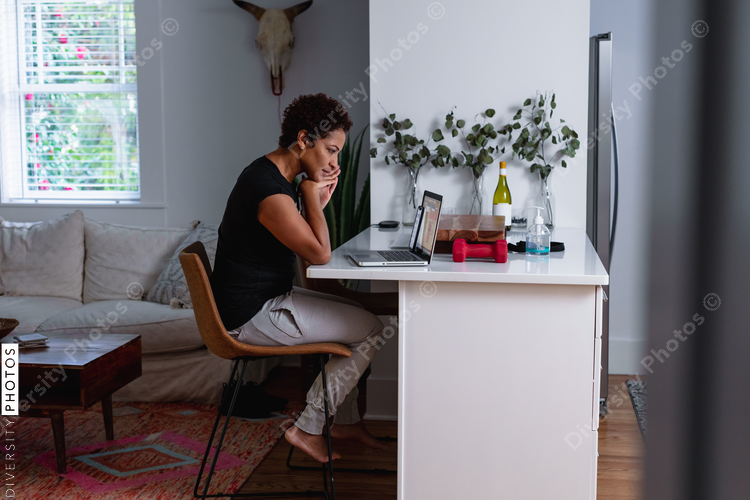 African-American woman works on laptop in home kitchen