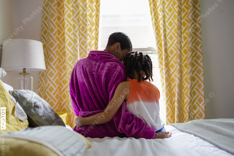Mother and daughter sitting on bed embracing, rear view