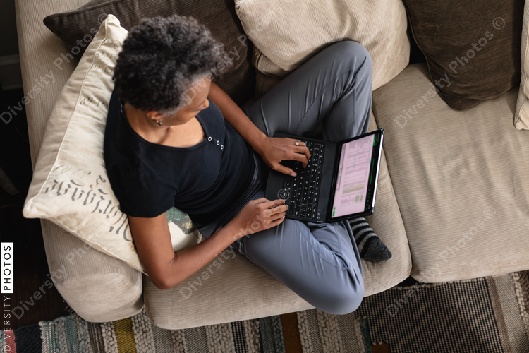 Overhead view of mature woman working from home on laptop, cozy and comfortable