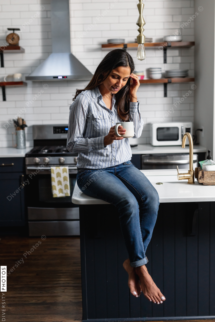 Young Indian woman sitting on kitchen counter, with tea drink