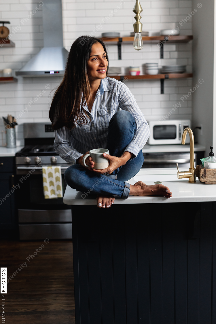 Young Indian woman sitting on kitchen counter, with tea drink