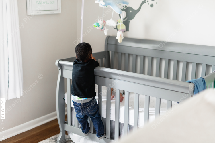 Big brother checking on sibling in crib, crying baby