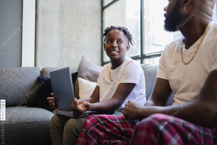African American Father and son with laptop sitting on sofa in living room