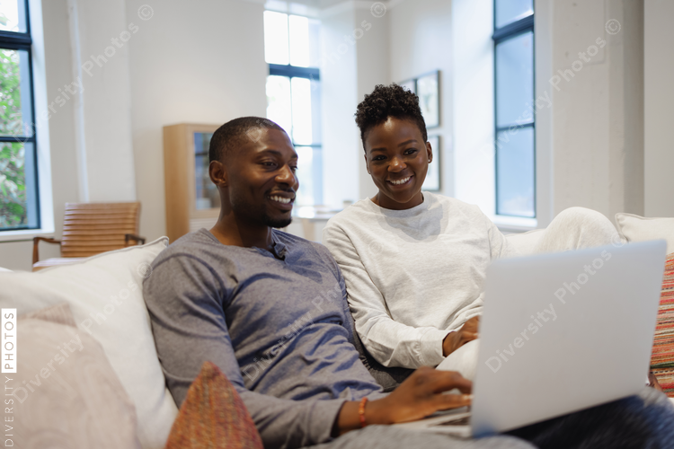 African American Smiling couple sitting on sofa and using laptop