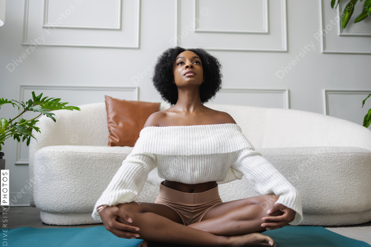 Young woman doing siddhasana yoga pose in living room