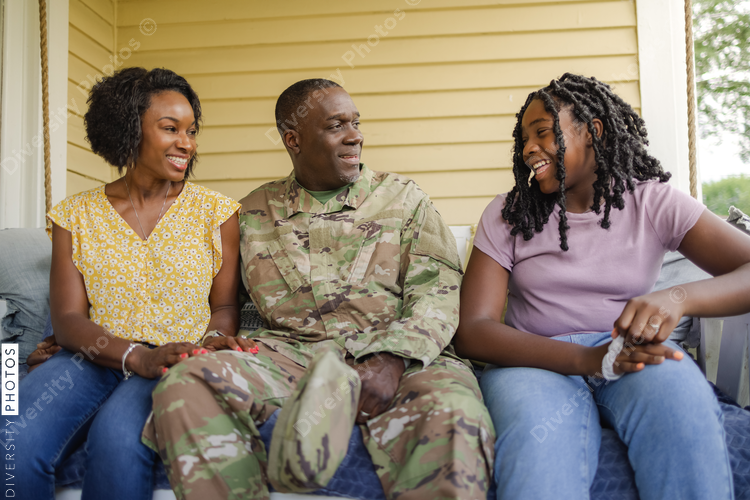 Military dad talks with wife and daughter on front porch swing, African American