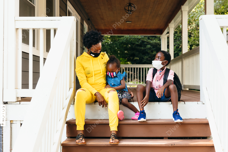 Mother with school age kids sitting on porch wearing masks as family