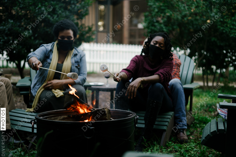 Black friends gathering around fire-pit roasting marshmallows and eating smores