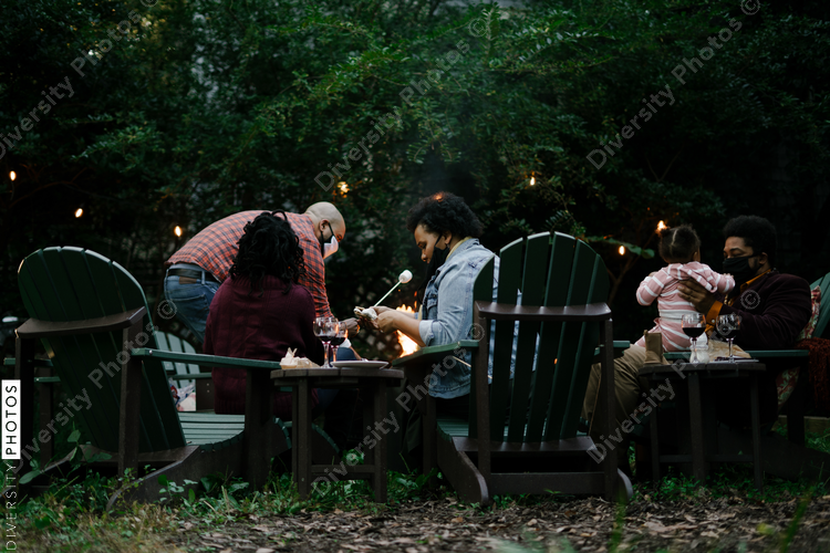 Black friends gathering around fire-pit roasting marshmallows and eating smores