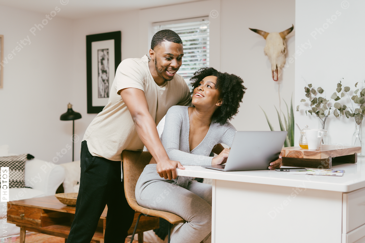 Smiling couple, boyfriend looks over girlfriend shoulder while she works on laptop, intimate moment