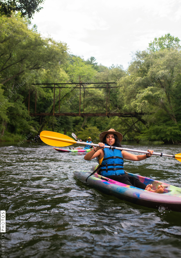 Woman kayaking on river with trees and footbridge in background