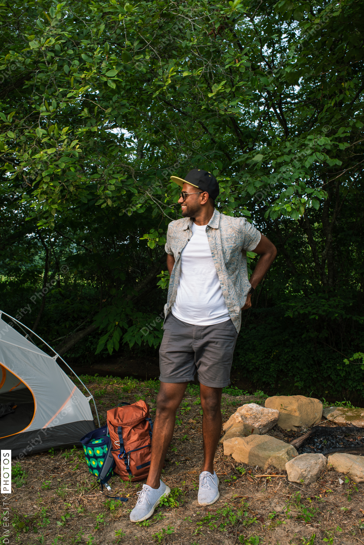 Smiling man standing next to tent on campsite
