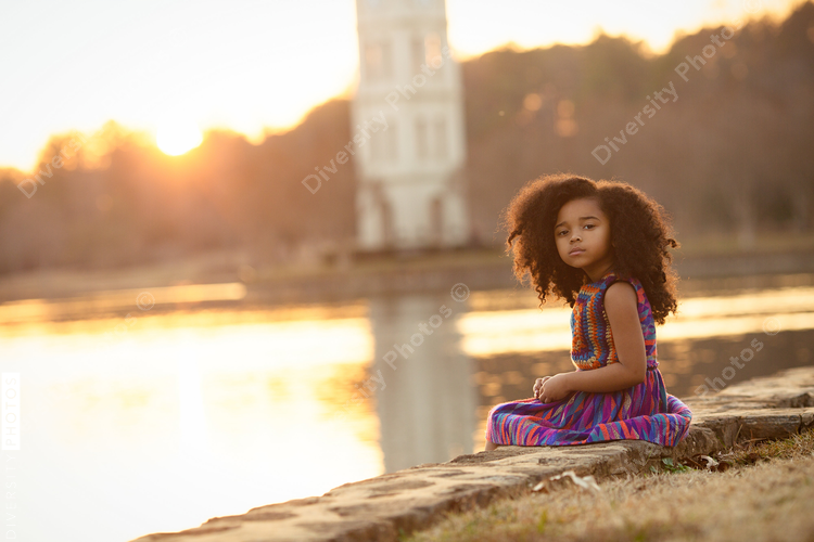 Portrait of girl sitting near lake during sunset