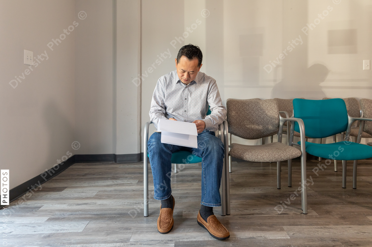 Asian man filling out patient forms at doctors office waiting area