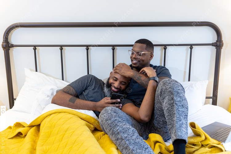 African American gay couple cuddling in bed at home, love is love connection