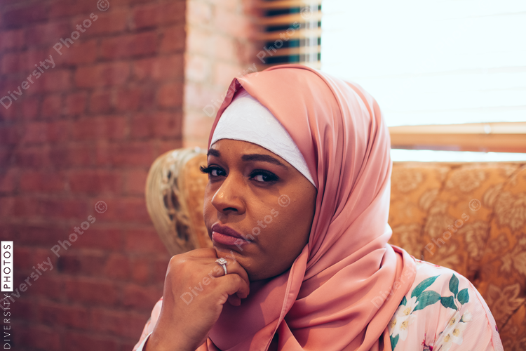 Portrait of thoughtful woman wearing hijab sitting in armchair