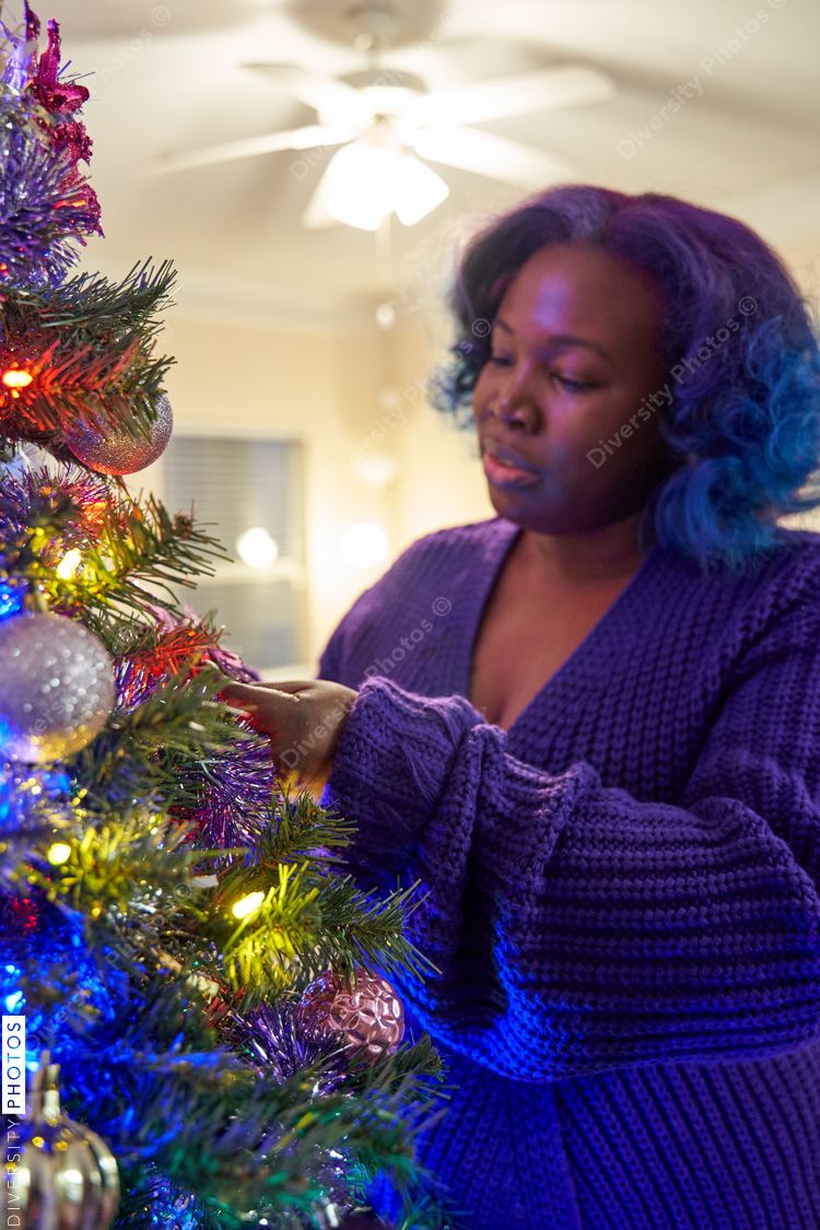 Black woman decorating Christmas tree at home, comfortable in robe