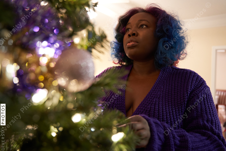 Black woman decorating Christmas tree at home, comfortable in robe