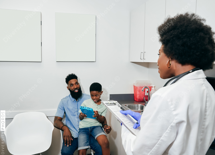 Black Pediatrician¬†with patients in her office taking notes