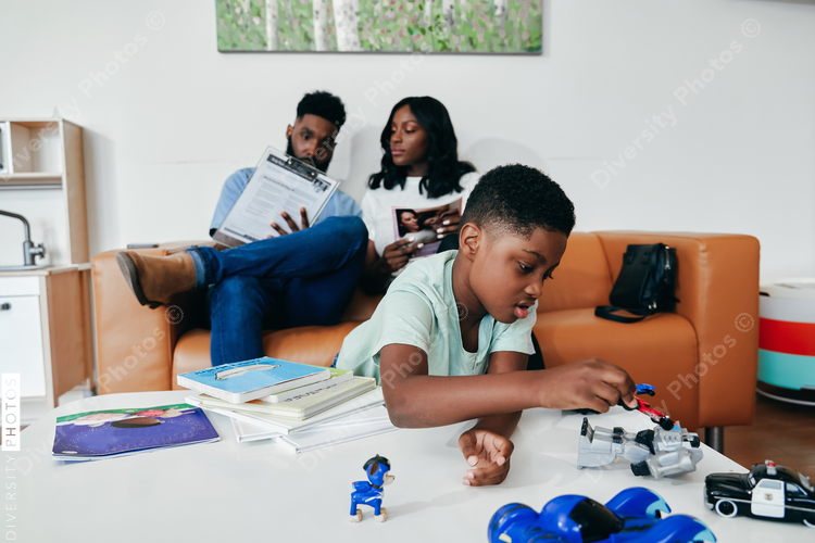 Black Family in clinic waiting room, kid plays with toys