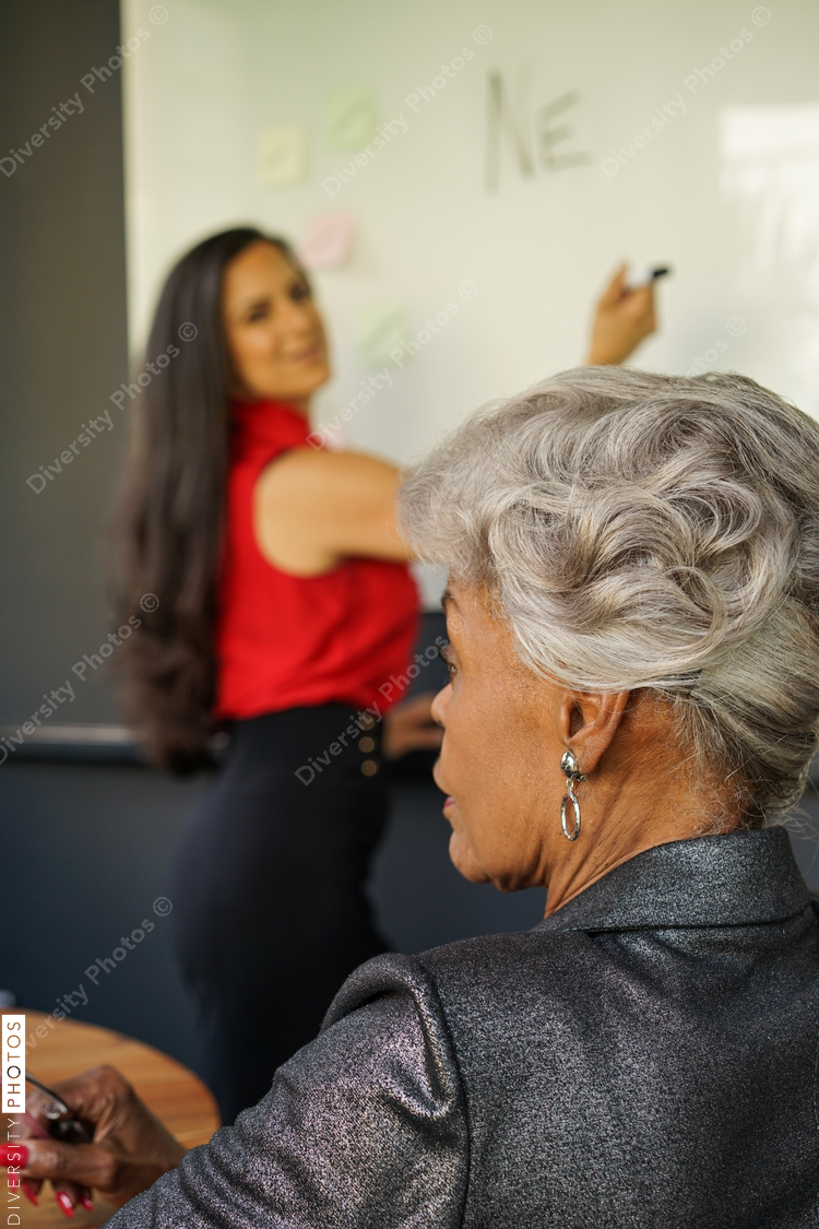 Businesswomen in meeting, colleague writing on whiteboard in background