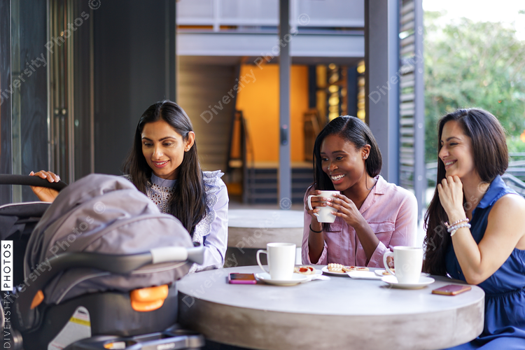 Smiling female friends looking at stroller in coffee shop