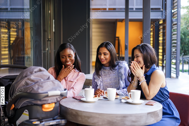 Smiling female friends looking at stroller in coffee shop