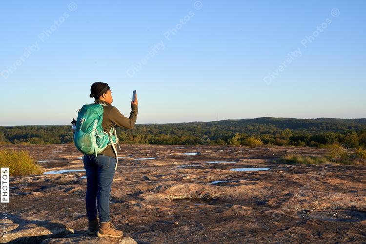 Black woman takes picture of beautiful mountain top view at sunset