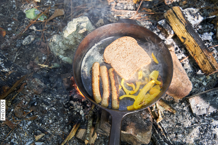 Breakfast being prepared over campsite fire in cast iron skillet