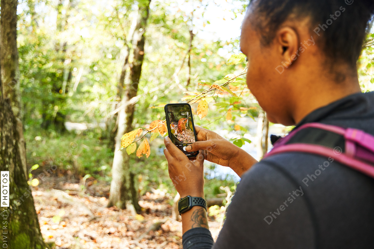 Black woman takes picture of leaves in woods for research