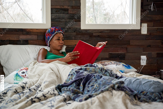 African American woman reading book in bed
