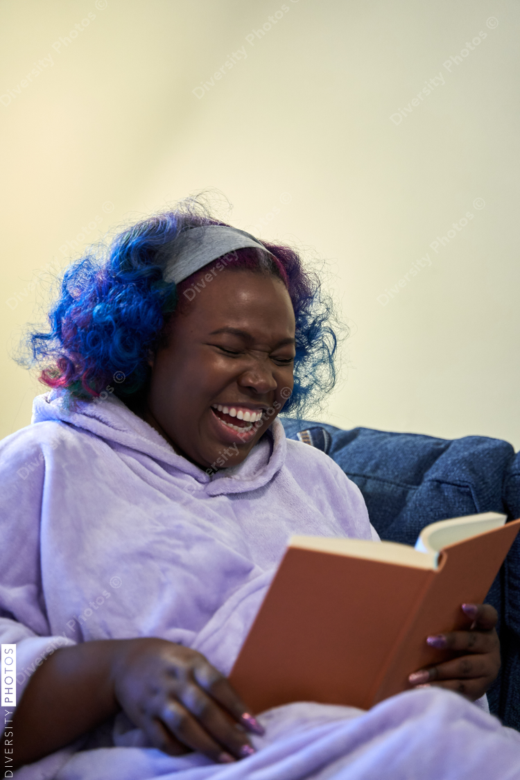 Black woman enjoying book at home, laughing, cozy and comfortable