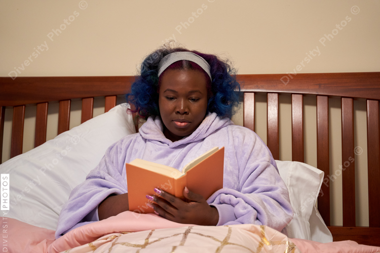 Black woman reading a book in bed, cozy