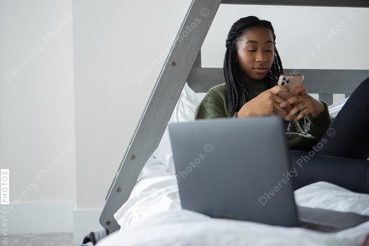 African American teen girl texting friends on cellphone at home in bedroom