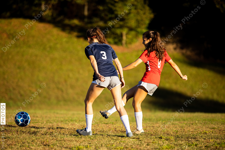 Teenage girl kicks soccer ball to teammate