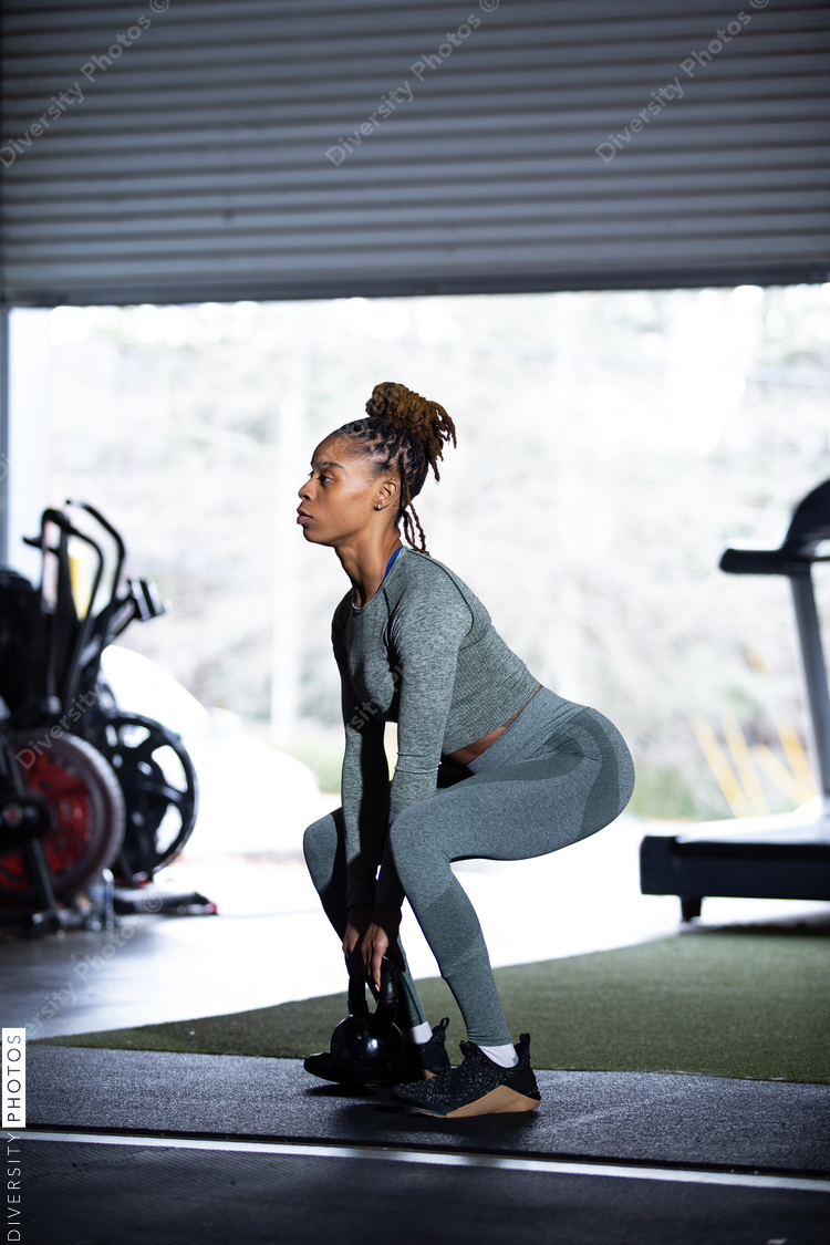 Black woman does exercises in gym, squat, kettleball swing