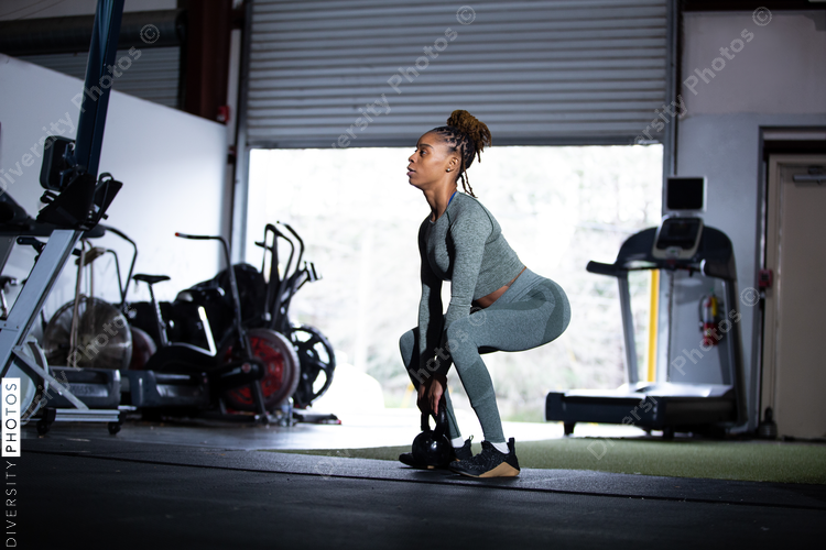 Black woman does exercises in gym, squat, kettleball swing