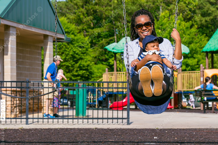 Smiling mother and baby son on playground swing