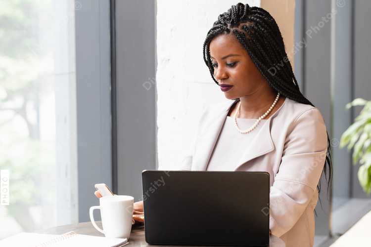 Businesswoman looks at phone next to laptop