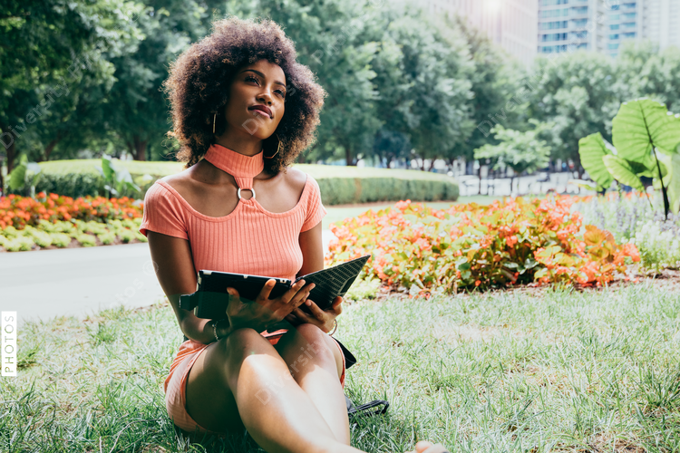 Black woman holding tablet while sitting park
