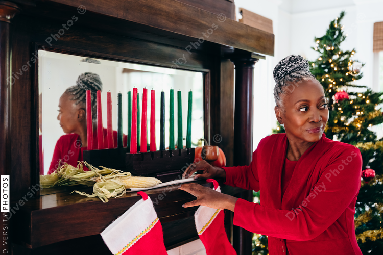 Senior Black woman setting up the Kwanzaa holiday setting and kinara with Christmas tree in background