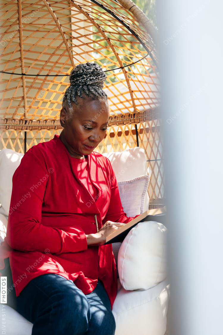 Senior Black woman with grey hair sitting outside and reading book
