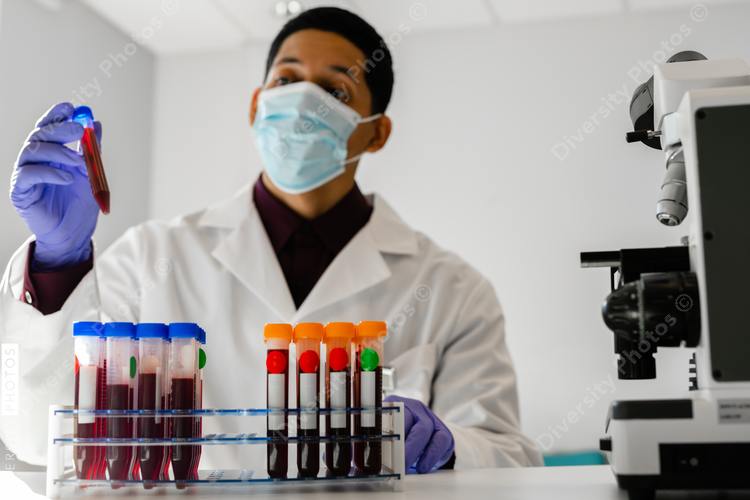Latino technician with blood test tube samples in laboratory with microscope equipment
