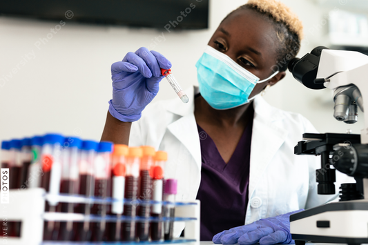 Black female scientist in mask in laboratory with test tubes and microscope equipment