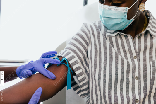 Black nurse collects blood sample from black female patient in exam room at medical facility