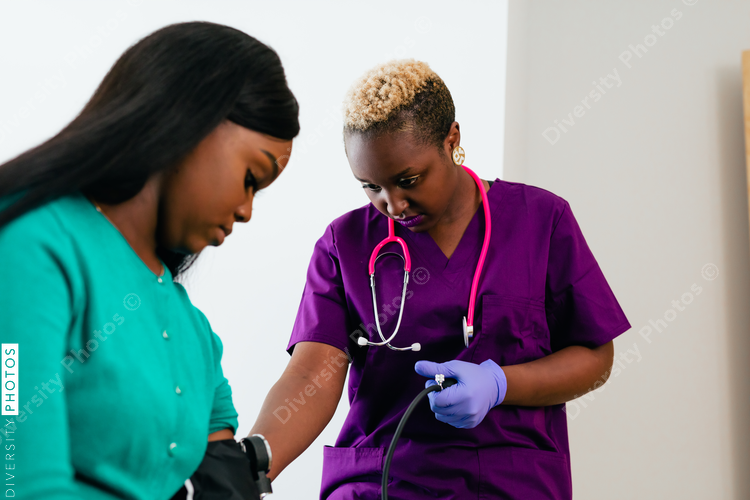 Black nurse takes blood pressure of black female patient in exam room at doctors office