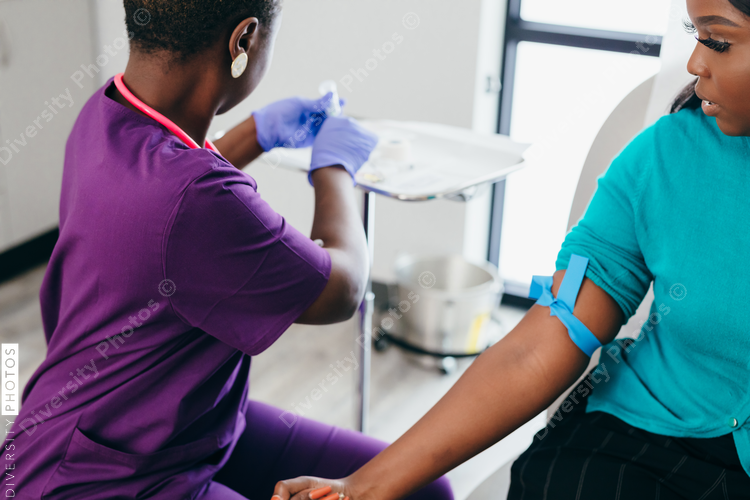 Black nurse collects blood sample from female patient at doctors office